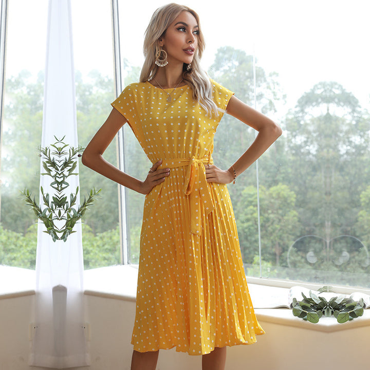 Woman wearing a yellow polka dot dress standing in a room with large windows.