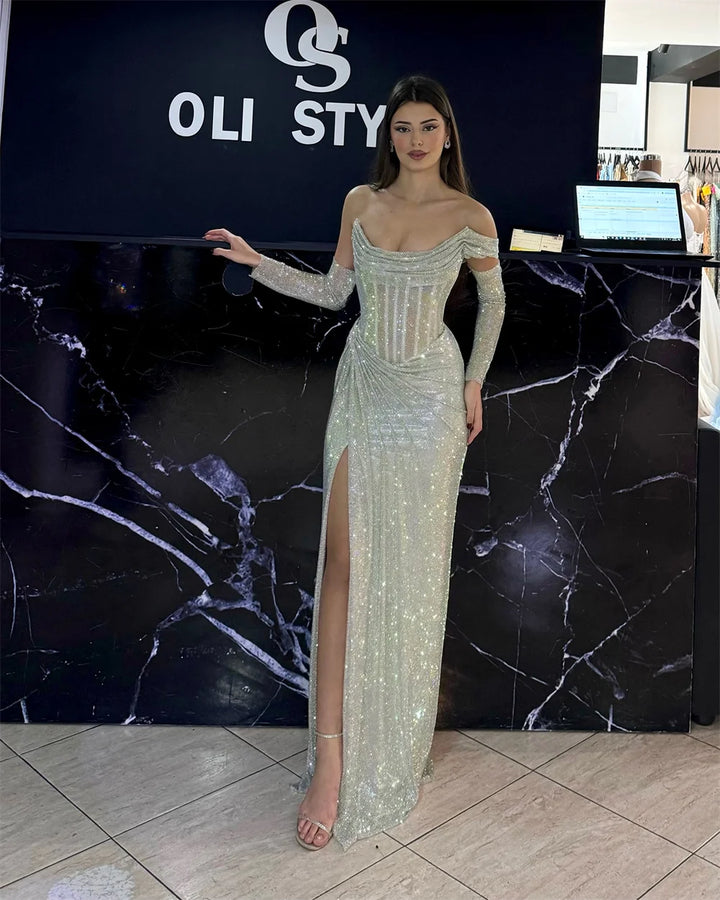 Woman in a sparkly off-shoulder gown standing in front of an OLI STYEL sign.
