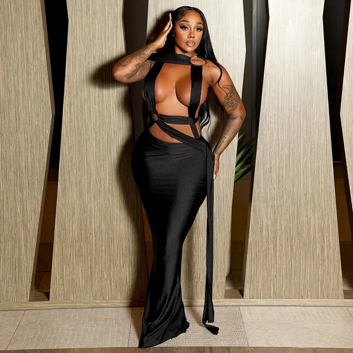 Woman wearing a black evening gown with sheer panels against a neutral wall.