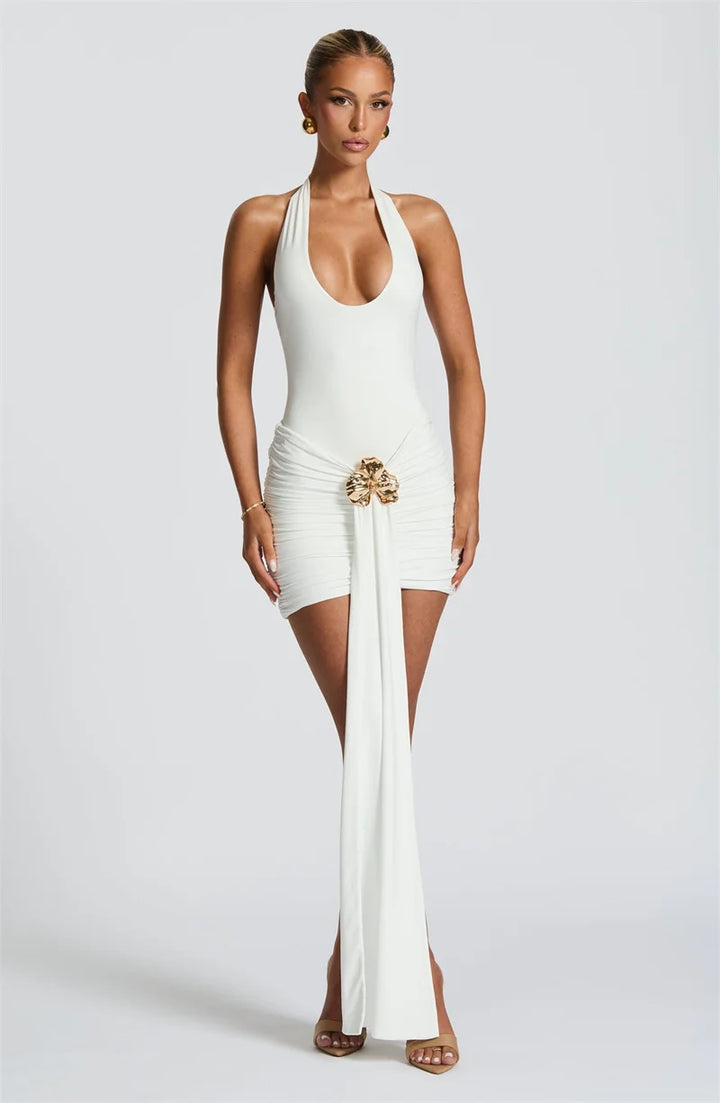 Woman wearing a white halter neck dress with a gold belt on a light gray background