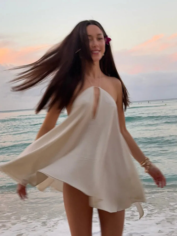 Woman in a white dress standing on a beach with a sunset in the background