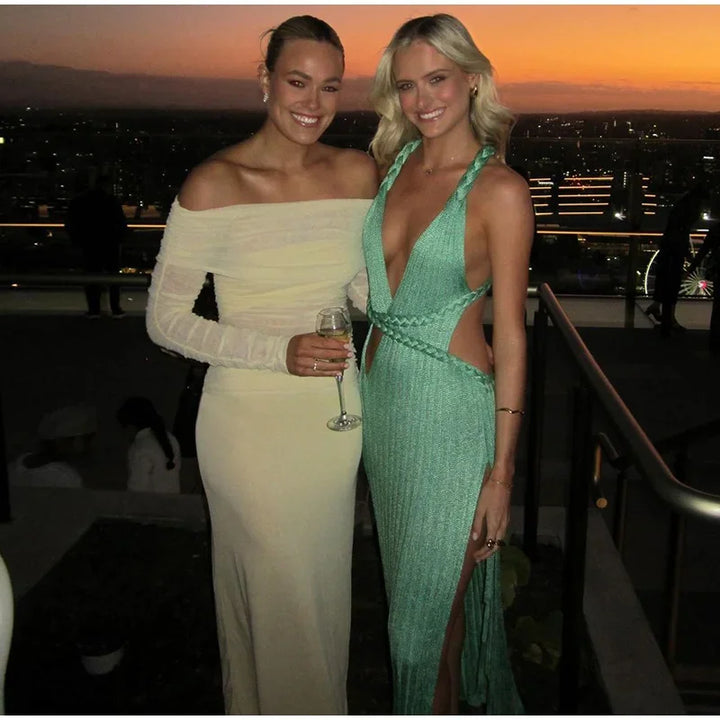Two women in elegant dresses standing together with a cityscape background at sunset.